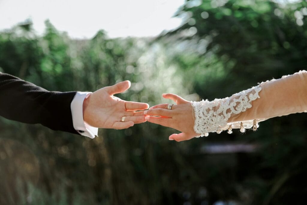A couple gently reaching for each other's hands during their outdoor wedding ceremony.