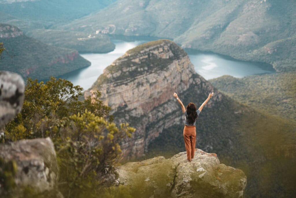 Woman with arms raised celebrating nature at Blyde River Canyon, South Africa.