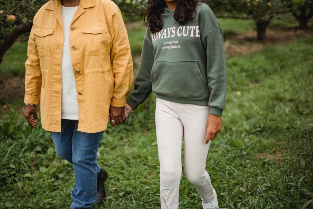 A mother and daughter walking hand in hand outdoors, enjoying a sunny day in nature.